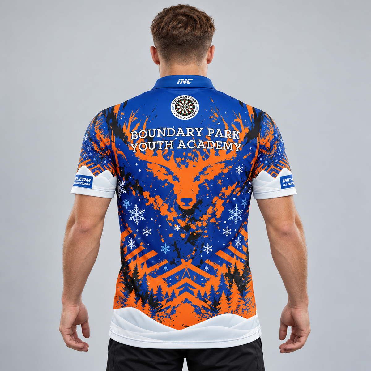 Back view of the TRADE Official Boundary Park Youth Darts Academy Christmas Shirt displaying prominent Boundary Park Youth Academy back text, circular crest on upper neck, INC collar logo, winter graphic pattern, and illegitiminoncarborundum text across the lower hem